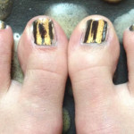 A person's toe nails with gold and black stripes.