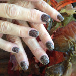 A woman's nails with black and brown glitter on them.