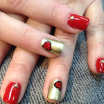 A woman's nails with red and gold hearts on them.