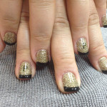 A woman's nails with gold and black glitter on them.