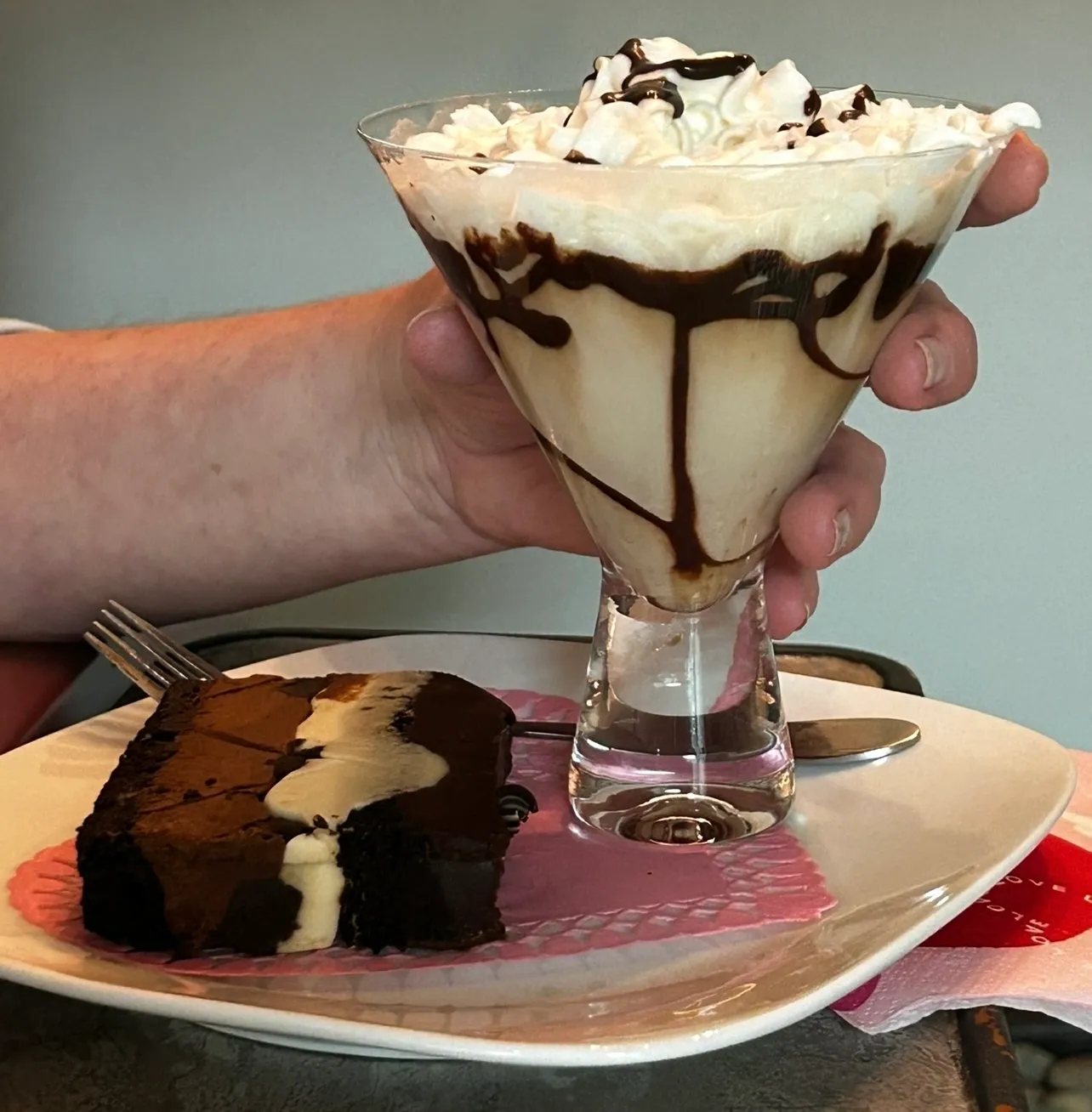 A person holding a glass of chocolate milk and cake.