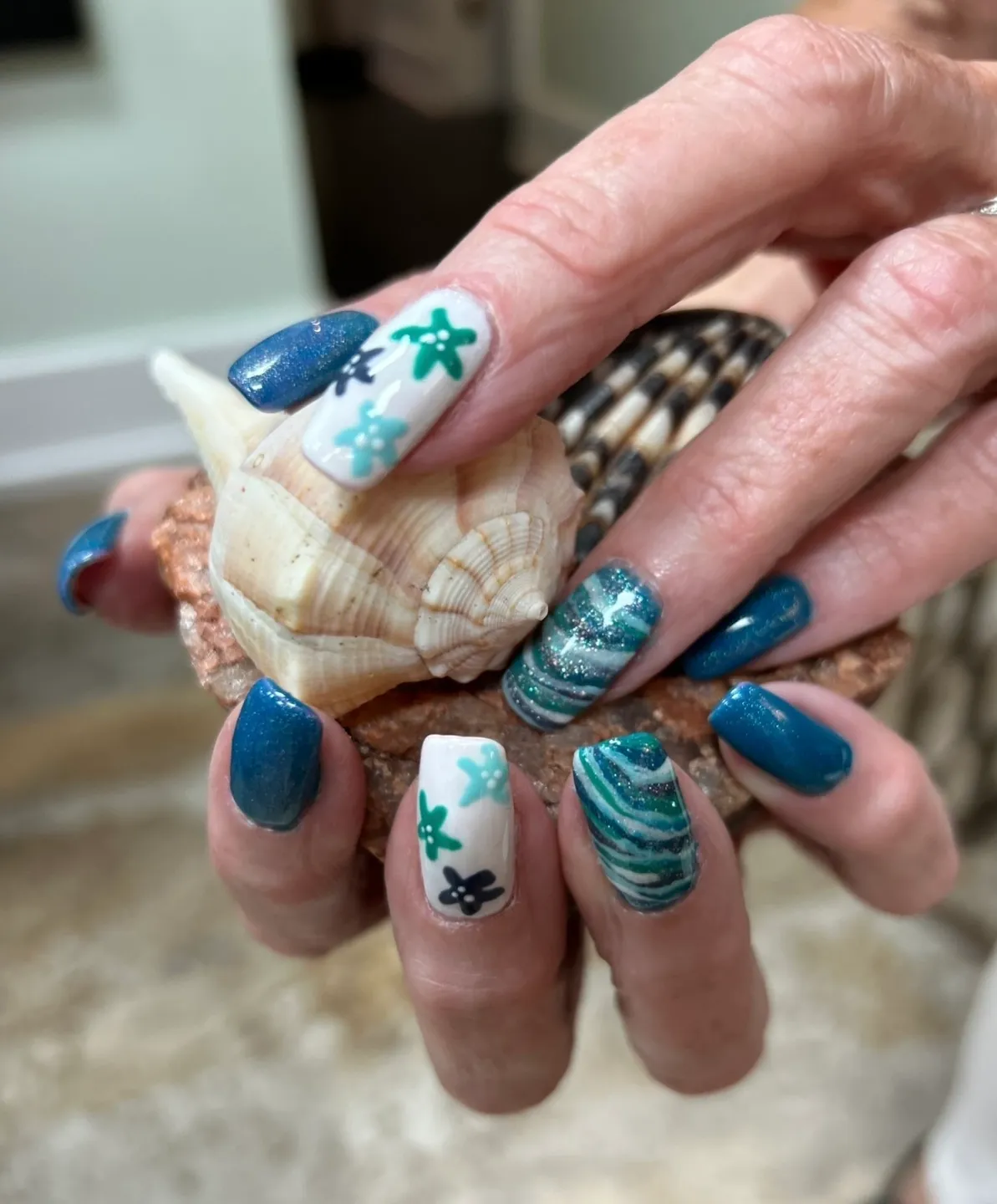 A woman holding a shell with blue and white nail art.