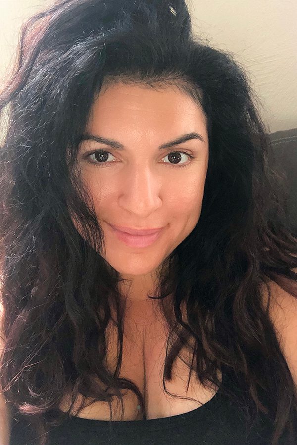 A woman with long hair and no bra is smiling.